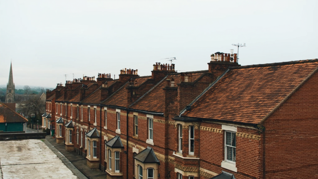 Row of red-brick Victorian terraced houses with orange clay tiled roofs and chimneys, a church spire in the distance
